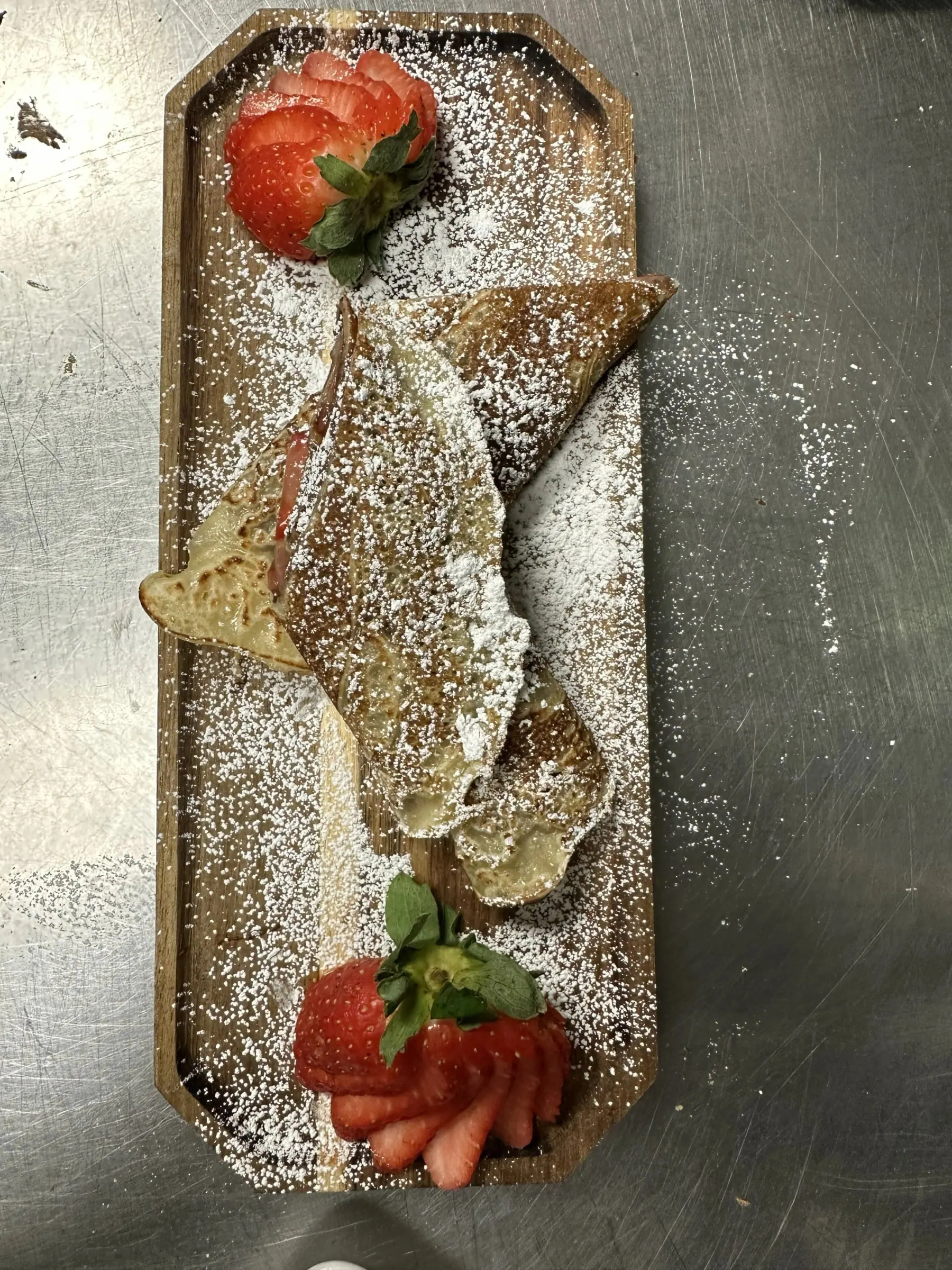 A folded crepe dusted with powdered sugar and served with fanned fresh strawberries