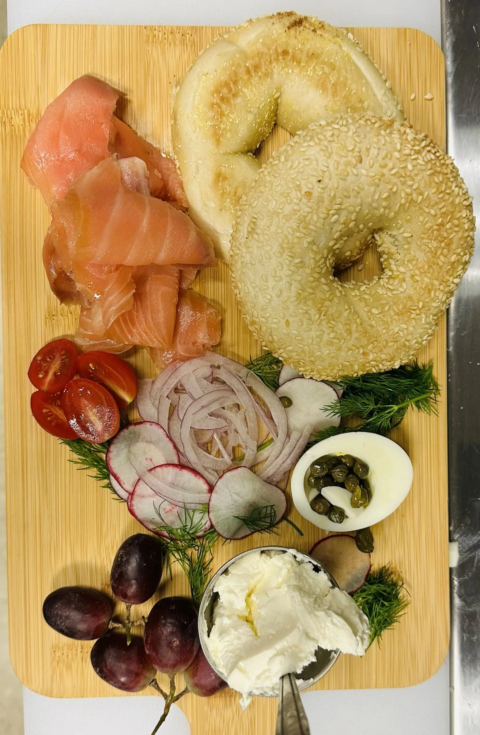 A board of cold-smoked salmon with sesame bagels, whipped cream cheese, capers, radish, tomato and dill