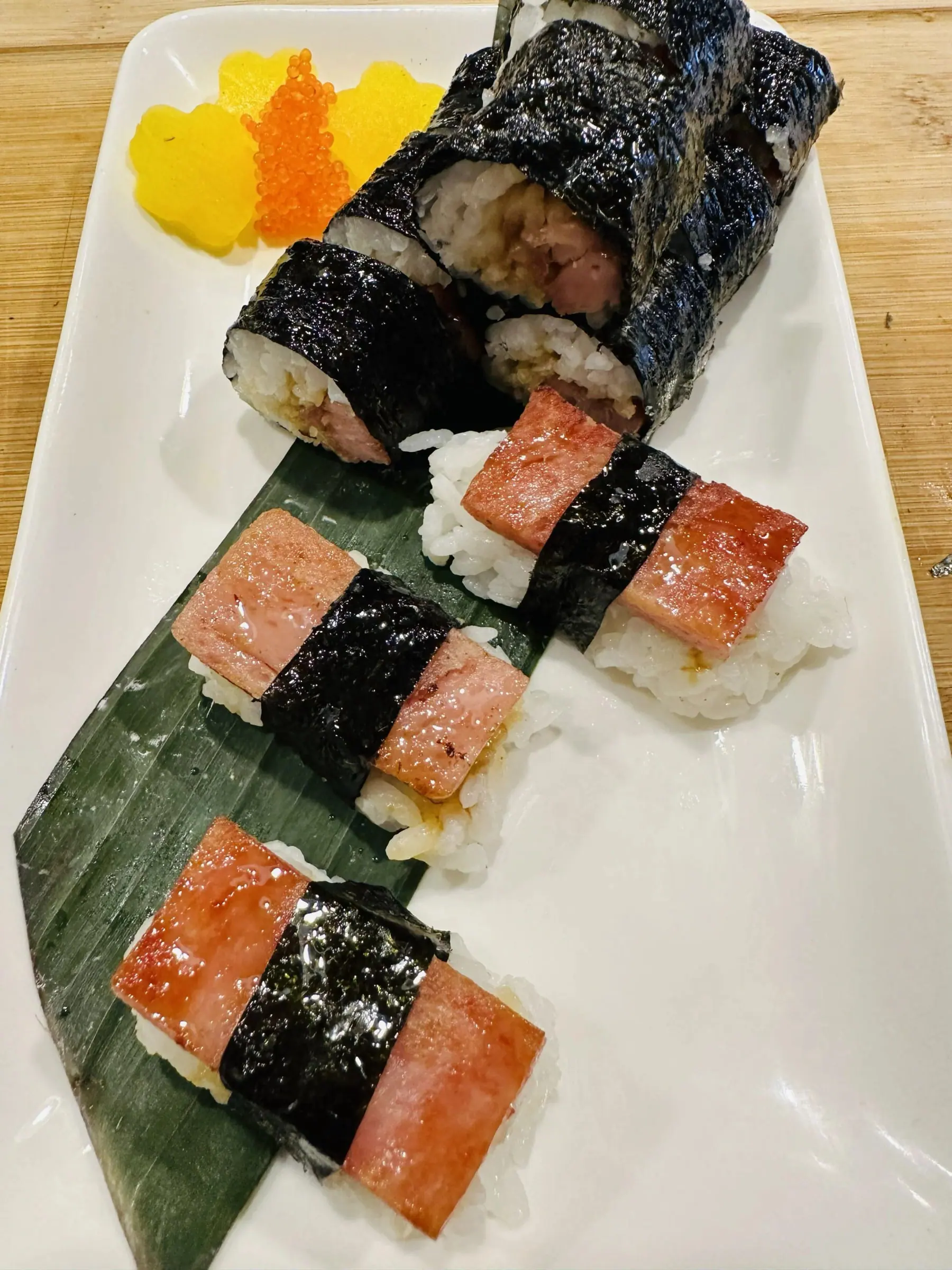 Nori-wrapped rice rolls and musubi with tobiko and pickled garnish on a white plate