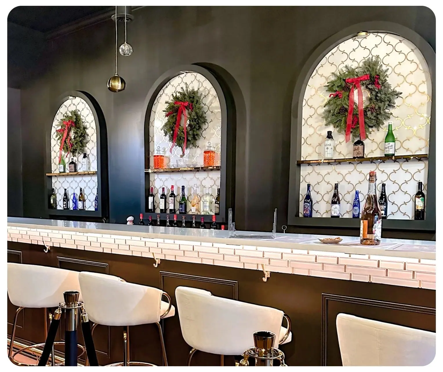 The main bar at The Bar on Baldwin: three arched niches backed with gold trellis tile, brass shelves of bottles and cream upholstered bar stools