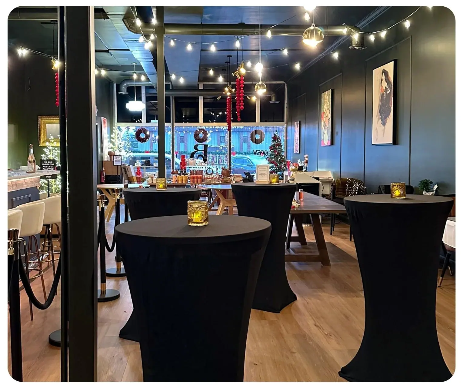 Black-draped cocktail tables under warm string lights at The Bar on Baldwin, with artwork on deep charcoal walls