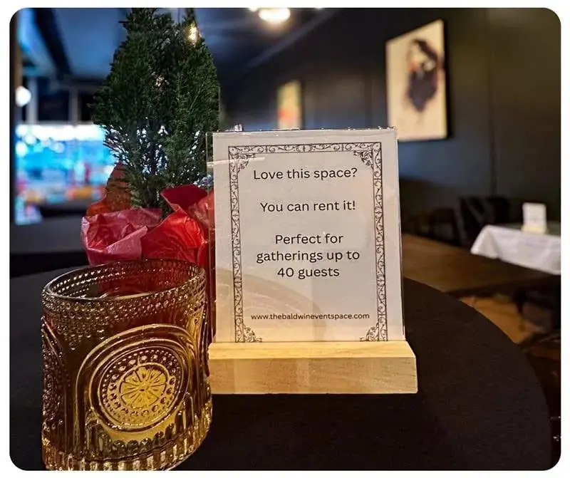 A table card at The Bar on Baldwin reading "Love this space? You can rent it! Perfect for gatherings up to 40 guests", beside a cut-glass amber tumbler